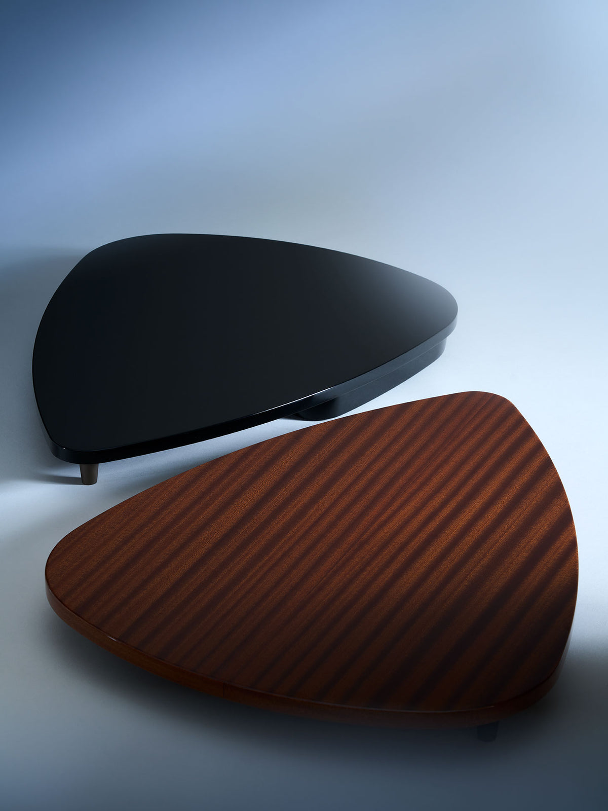 Two sculptural guitar stands in black and walnut wood with curved teardrop design, showcasing premium instrument display pieces
