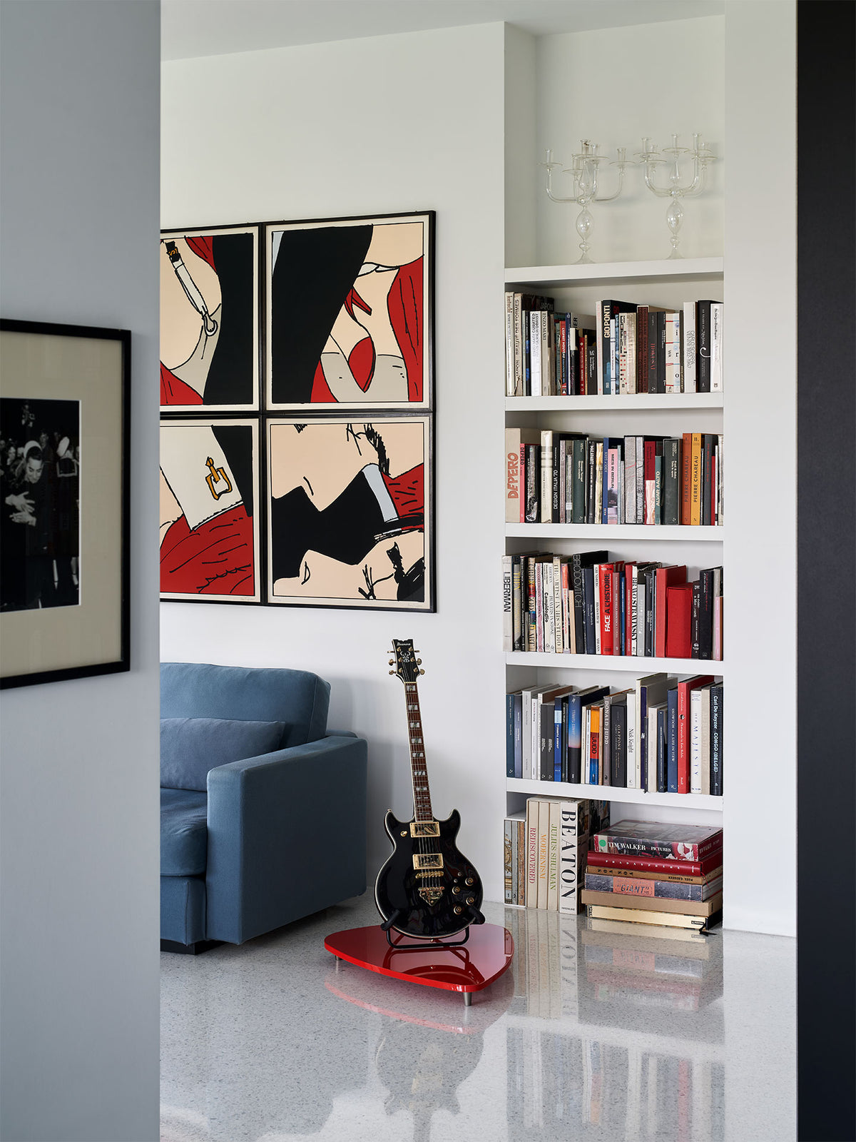 Black electric guitar on red stand displayed in modern interior with bookshelf and pop art wall decor